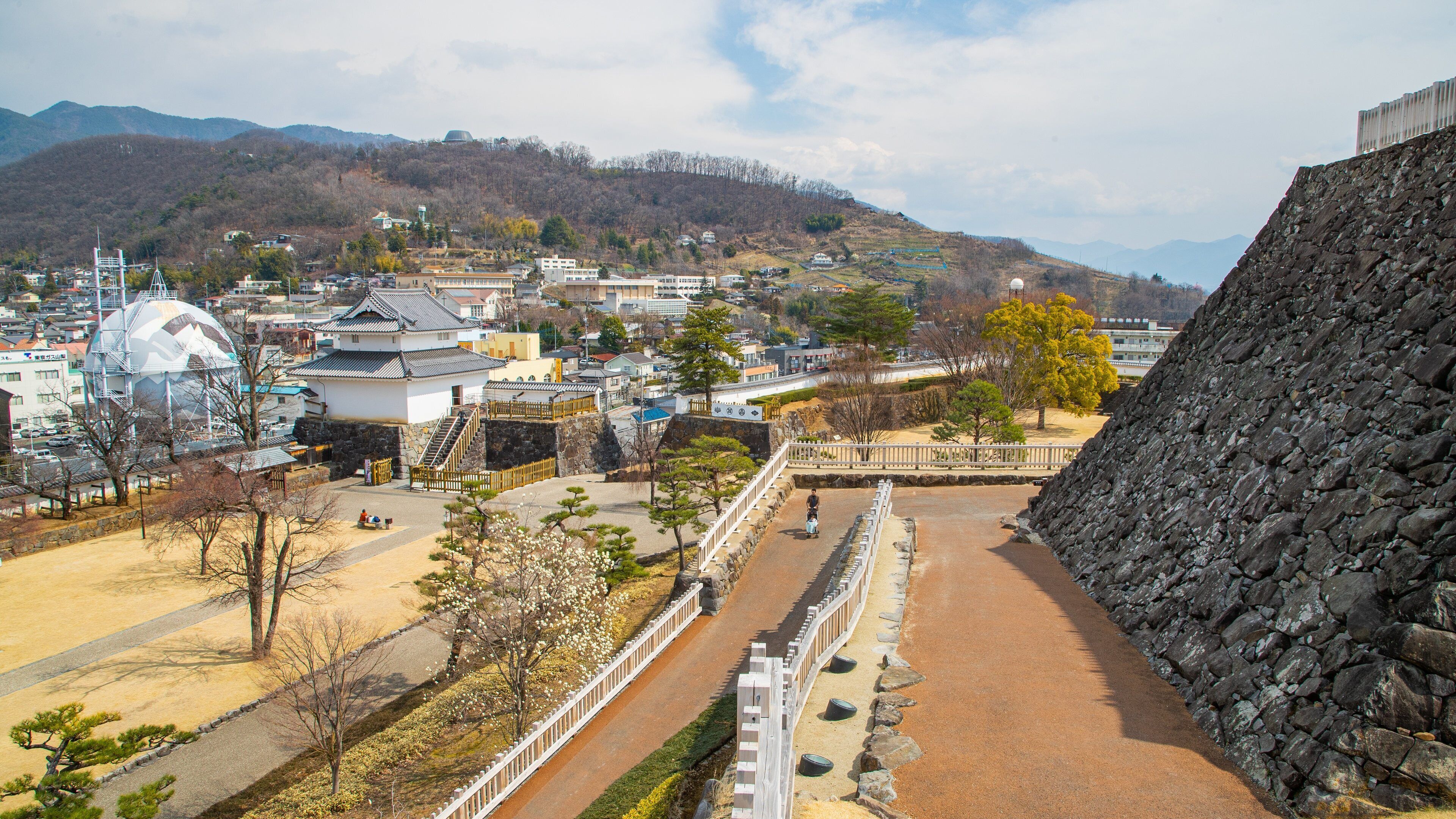 A traditional Japanese town with a stone wall, a large white building with a dome, and a river.