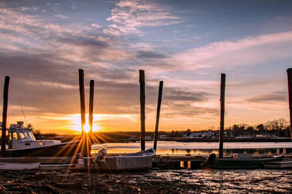 A sunset over a harbor with boats docked and a bridge in the foreground.