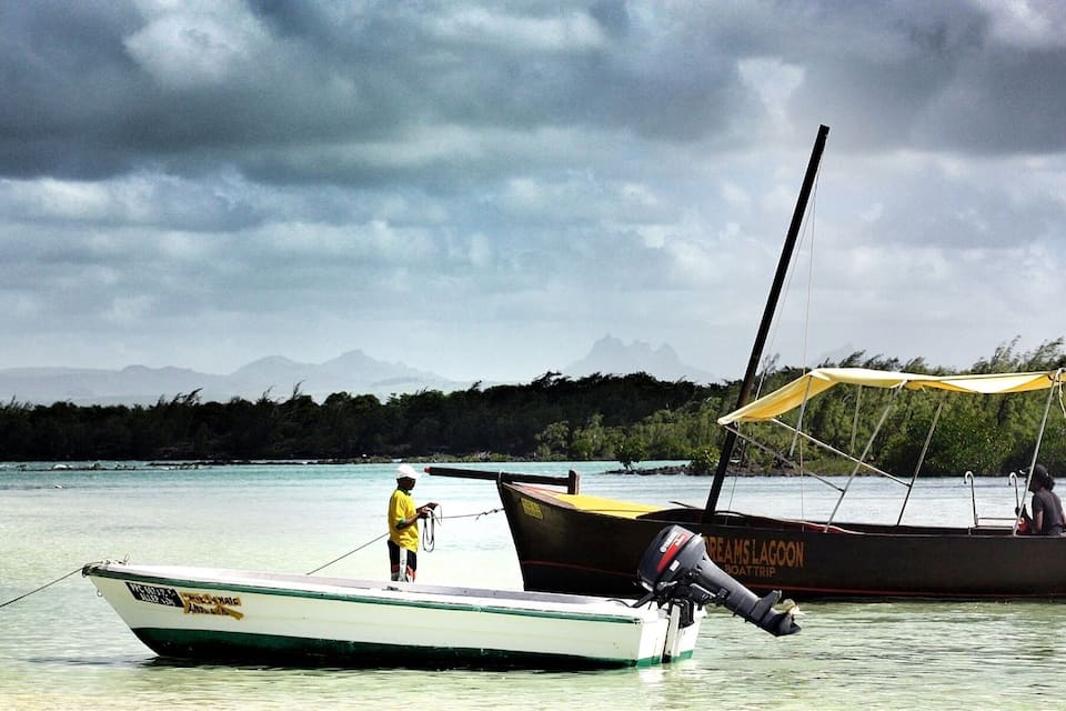 Dos barcos anclados cerca de una playa con montañas al fondo.
