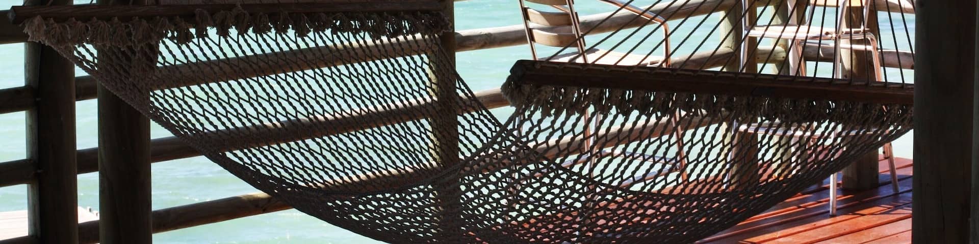 Una hamaca en una terraza de madera con vistas a aguas turquesas y una costa lejana.