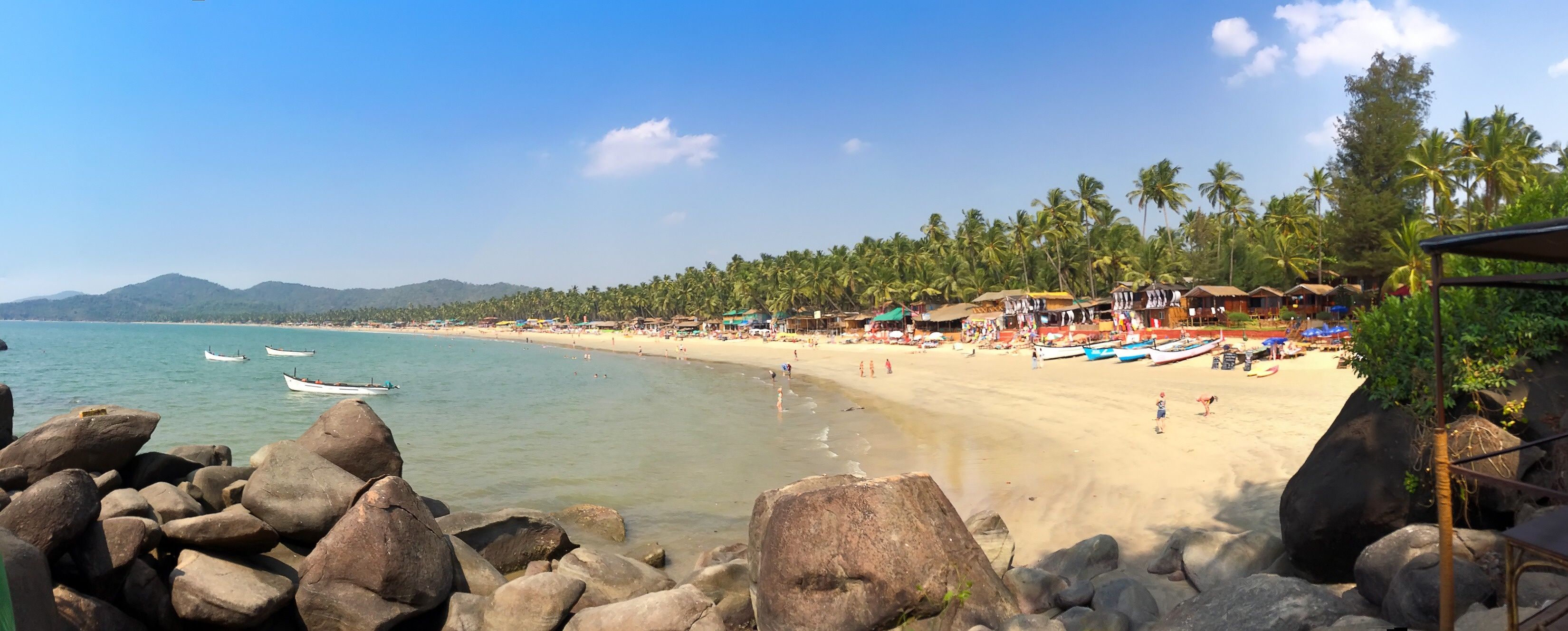 A tropical beach with clear turquoise water, rocky shoreline, palm trees, and beach umbrellas.