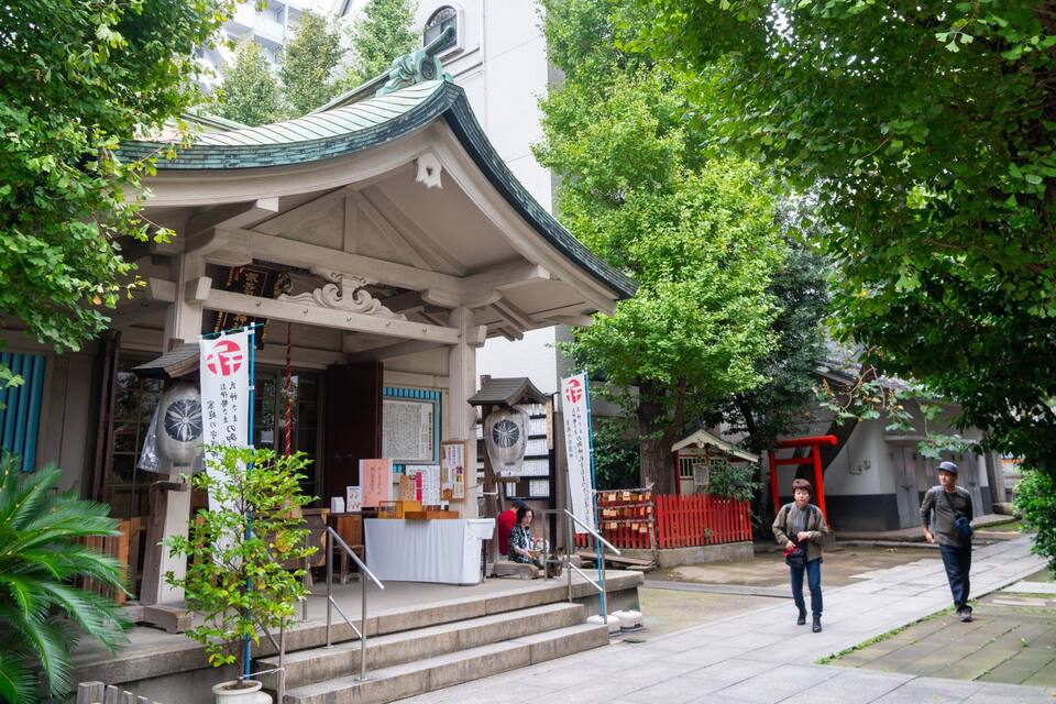A traditional Japanese shrine with a curved roof, surrounded by lush greenery and a red gate.
