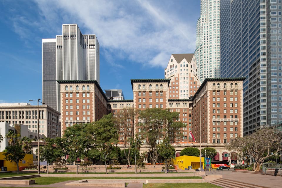 A cityscape with modern skyscrapers, historic buildings, and a park with trees and a yellow structure.