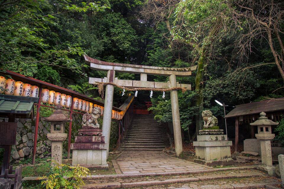 A traditional Japanese shrine with stone lanterns, a torii gate, and a staircase leading up to a shrine area.