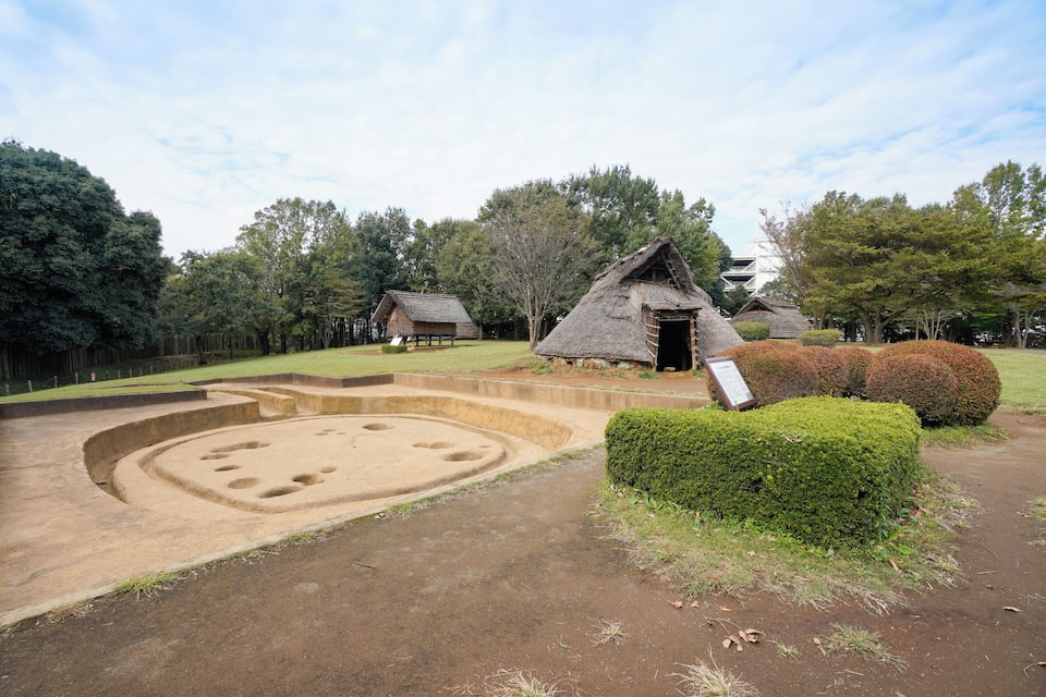 A traditional thatched-roof house surrounded by a landscaped garden with a circular earthwork feature.