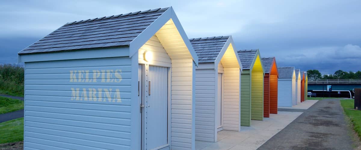 A row of brightly colored beach huts with the sign 'KELPIES MARINA' on the left.