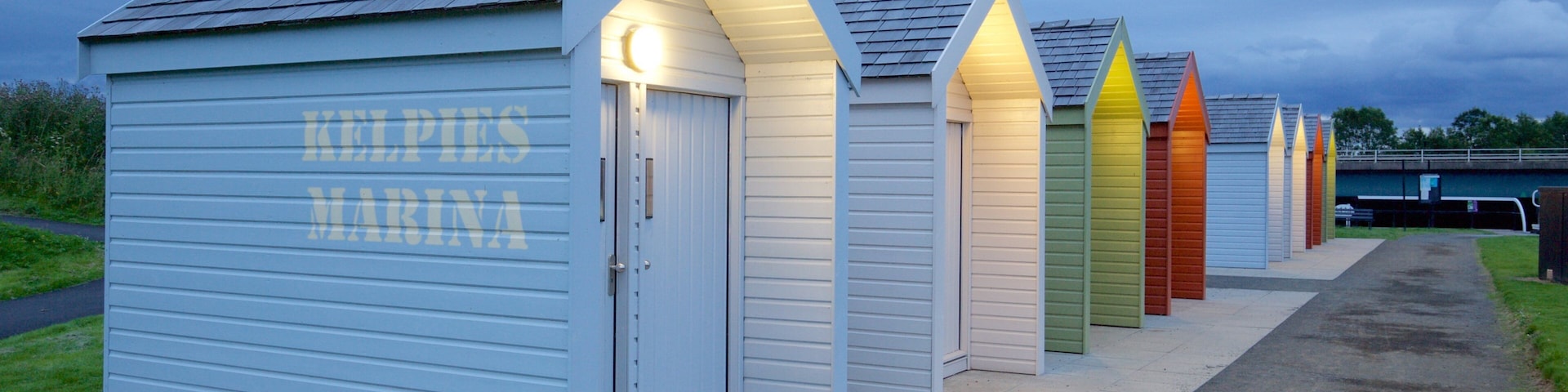 A row of brightly colored beach huts with the sign 'KELPIES MARINA' on the left.