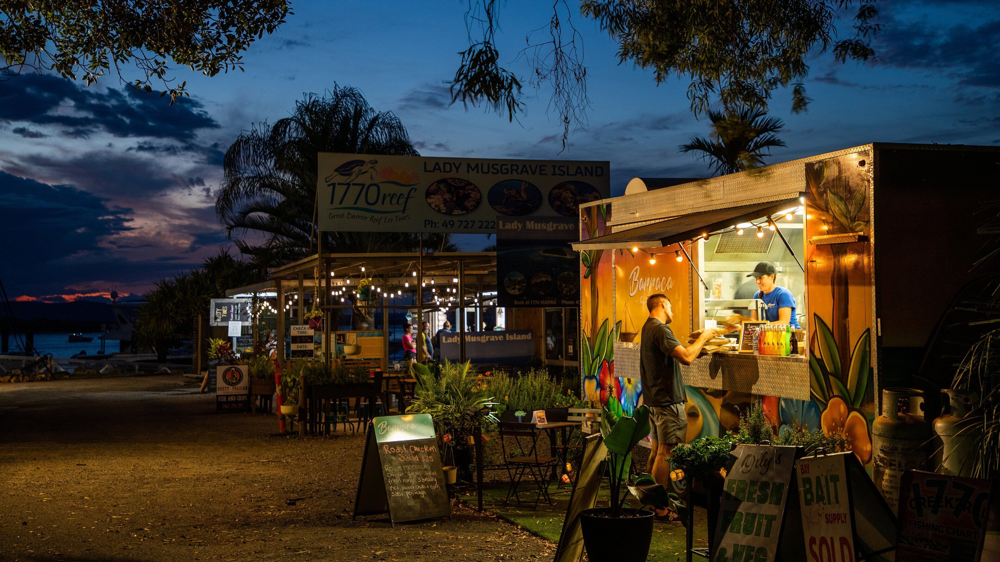 A food truck at dusk with a sign for 'Lady Musgrave Island' and a menu board.