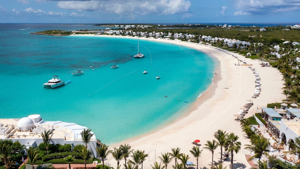 A turquoise beach with boats, a white sandy shore, and a resort area with palm trees.