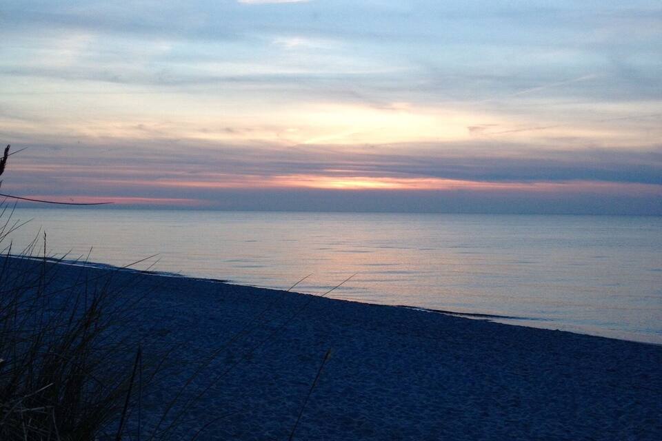 A beach at sunset with a clear sky and calm sea.