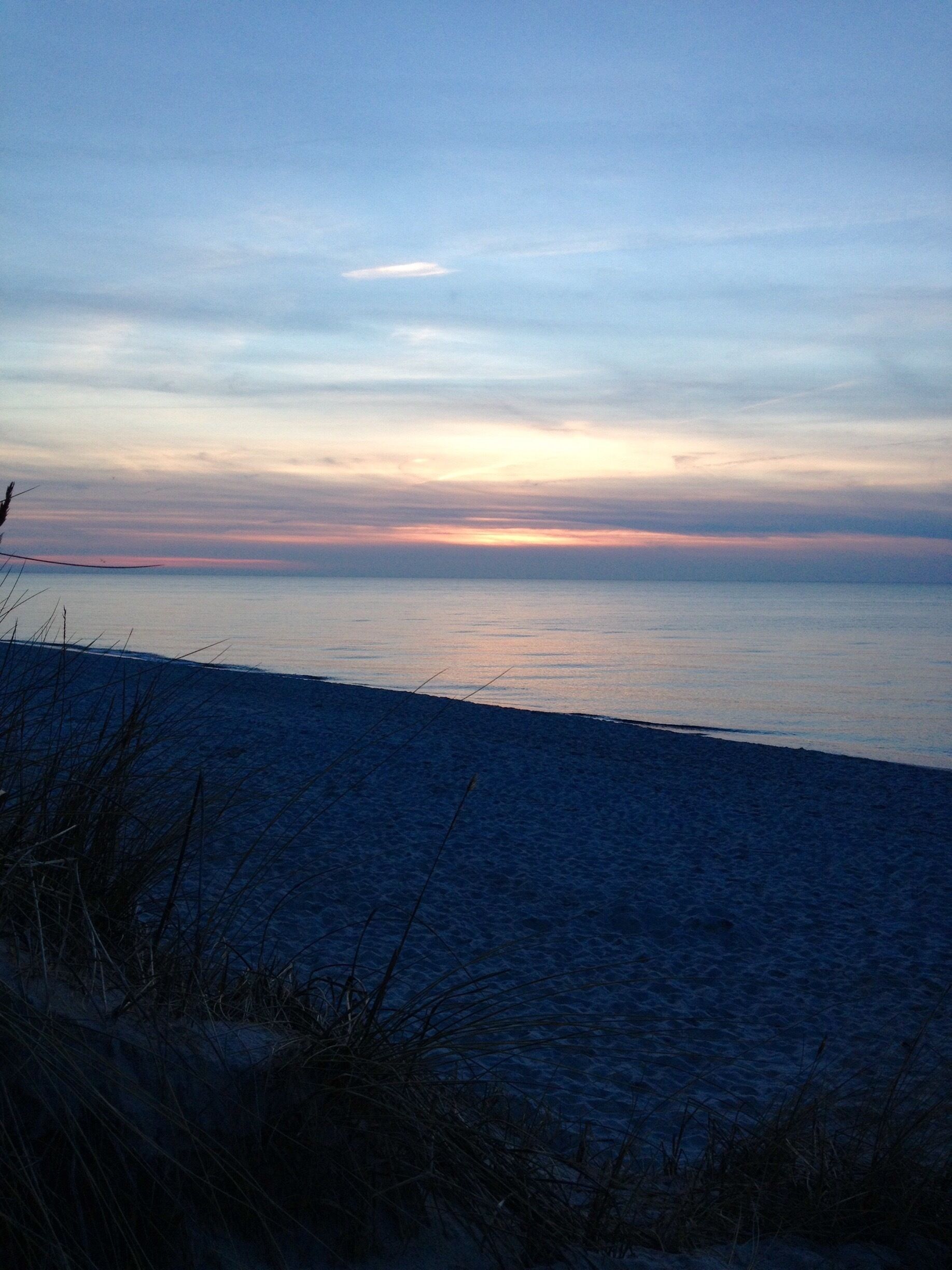A beach at sunset with a clear sky and calm sea.