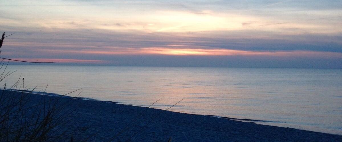 A beach at sunset with a clear sky and calm sea.