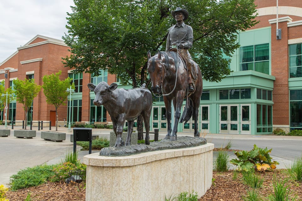 Estátua de um homem montado em um cavalo, com uma vaca na frente de um edifício com uma placa que diz 'CENTRE'.