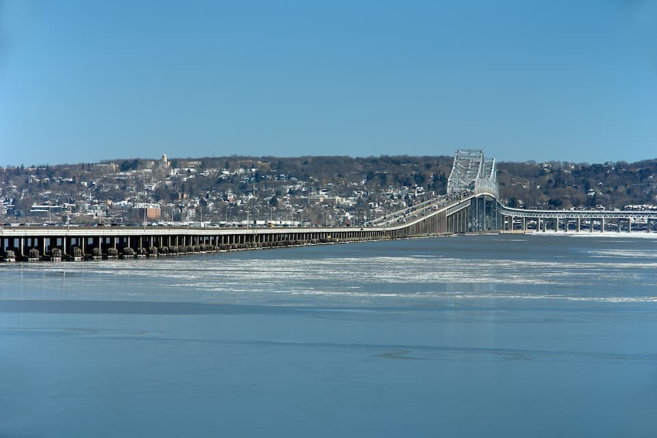 A bridge spanning a frozen river with a cityscape in the background.