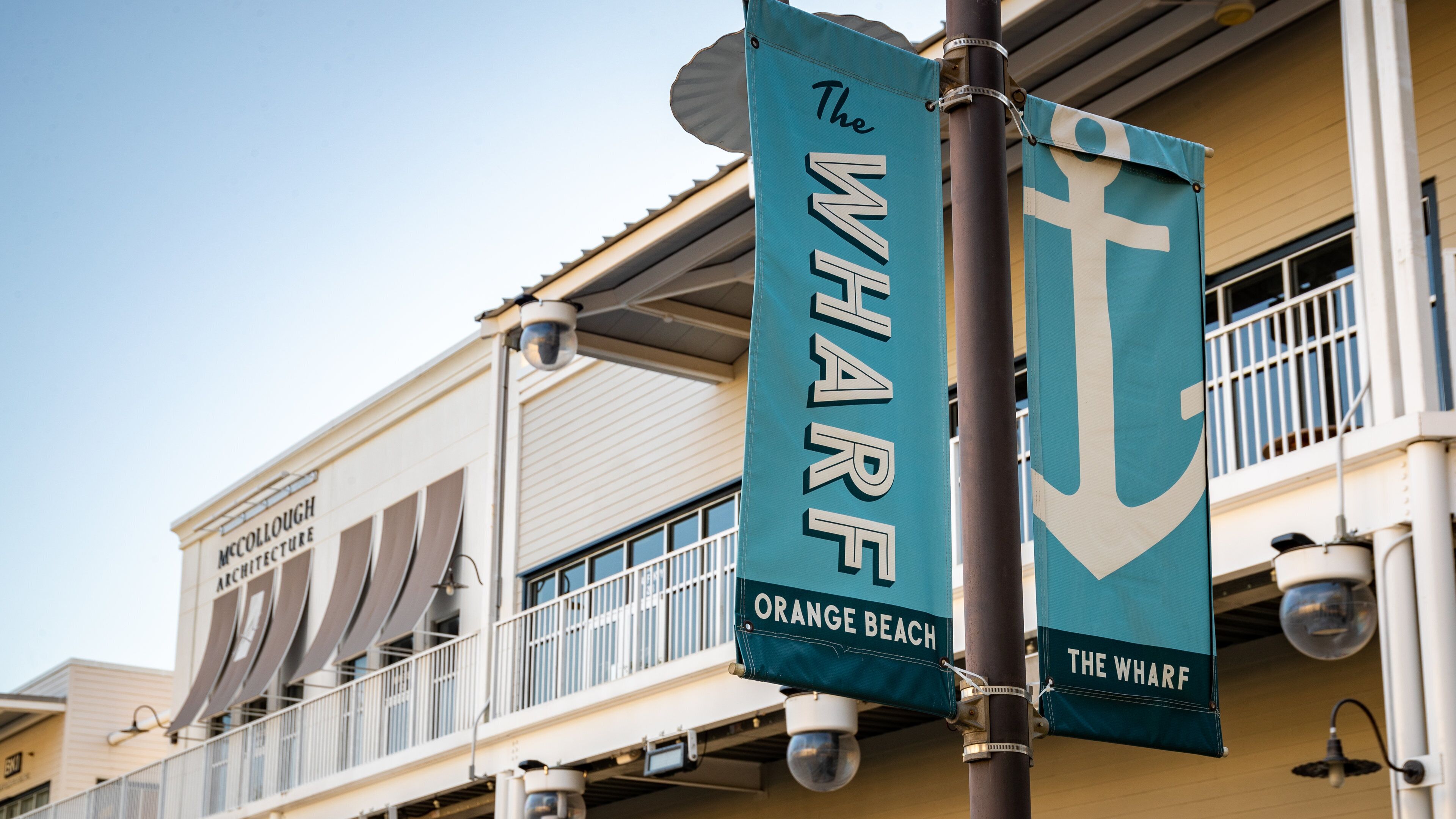 Twee vlaggen hangen aan een paal, één met de tekst 'The Wharf Orange Beach' en de andere met 'The Wharf'.
