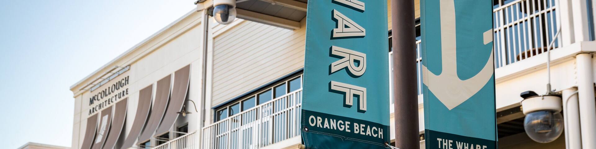 Two banners hanging from a pole, one reads "The Wharf Orange Beach" and the other "The Wharf".