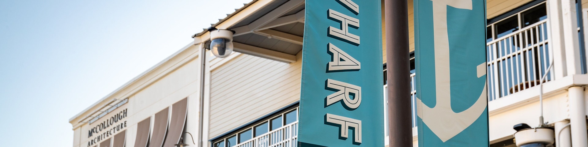 Dois banners pendurados em um mastro, um deles com a inscrição “The Wharf Orange Beach” e o outro com “The Wharf”.
