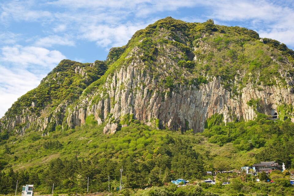 A mountainous landscape with dense green vegetation and traditional architecture at its base.