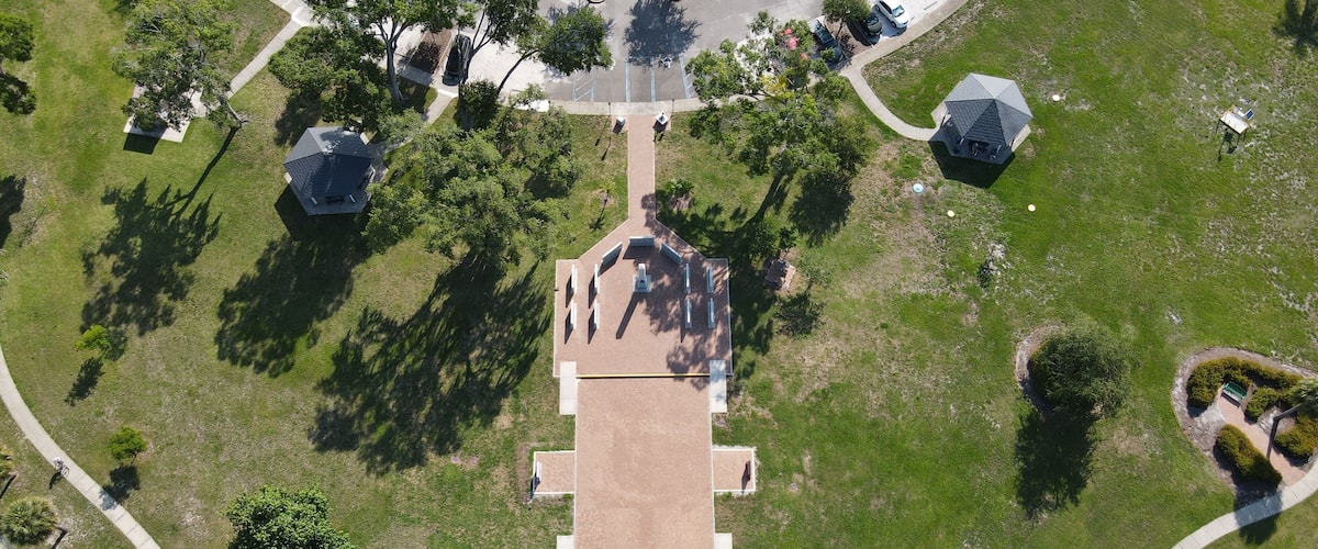 Drone photography of Veterans Memorial Park in Oldsmar, Florida, a waterside park featuring a memorial, a bocce court, fitness equipment, trails, and a gazebo in Tampa Bay