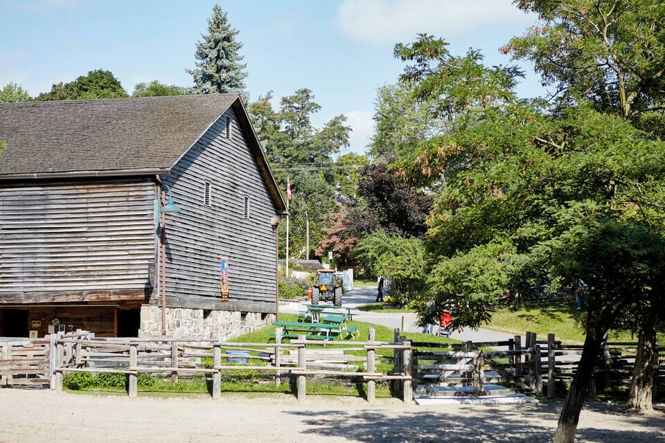 A rustic wooden barn with a stone foundation, surrounded by a wooden fence and picnic tables.