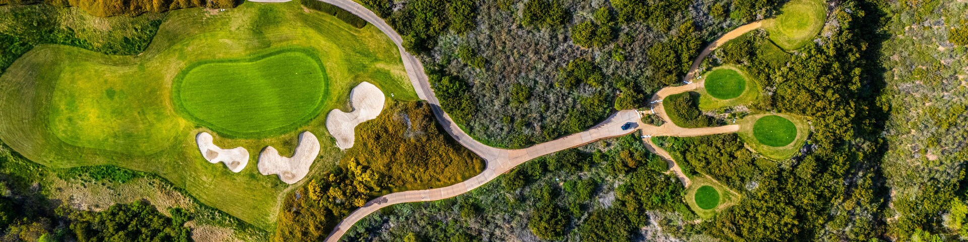 erial view of a golf course green with sand bunkers surrounded by natural shrubland in Newport Beach, California. The image captures a blend of manicured landscape and untamed wilderness, typical of S