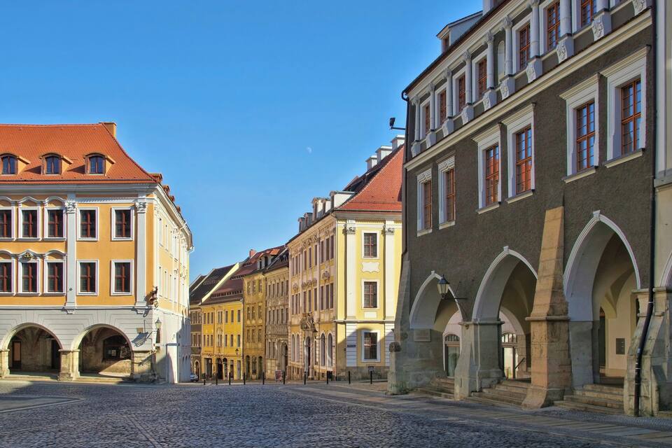 A cobblestone street lined with historic buildings featuring arched doorways and red-tiled roofs.