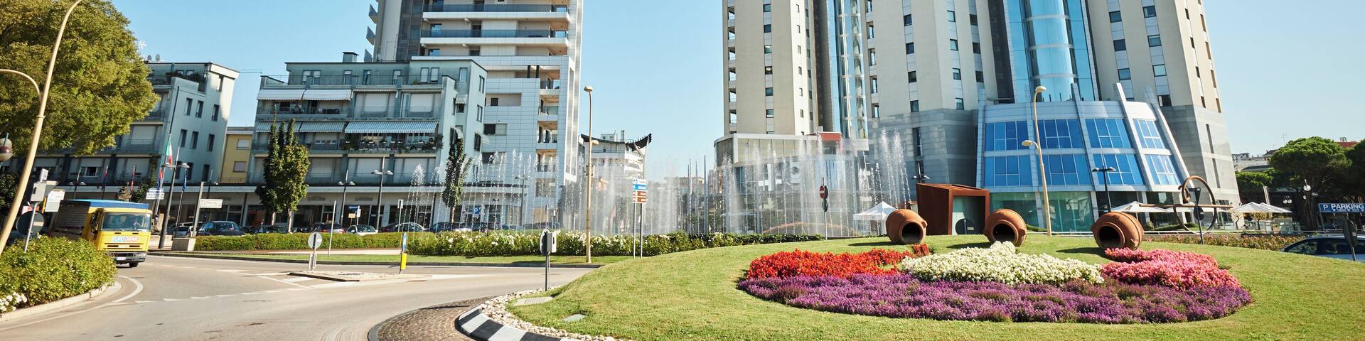 A modern urban landscape with a prominent skyscraper, a roundabout, and a flower garden.