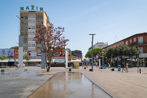 Ein Platz mit einem Brunnen, einem MAXIM Gebäude und verschiedenen Geschäften.