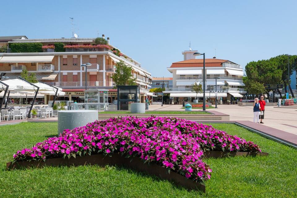 Una plaza pública con un parterre floral, asientos al aire libre y edificios al fondo.
