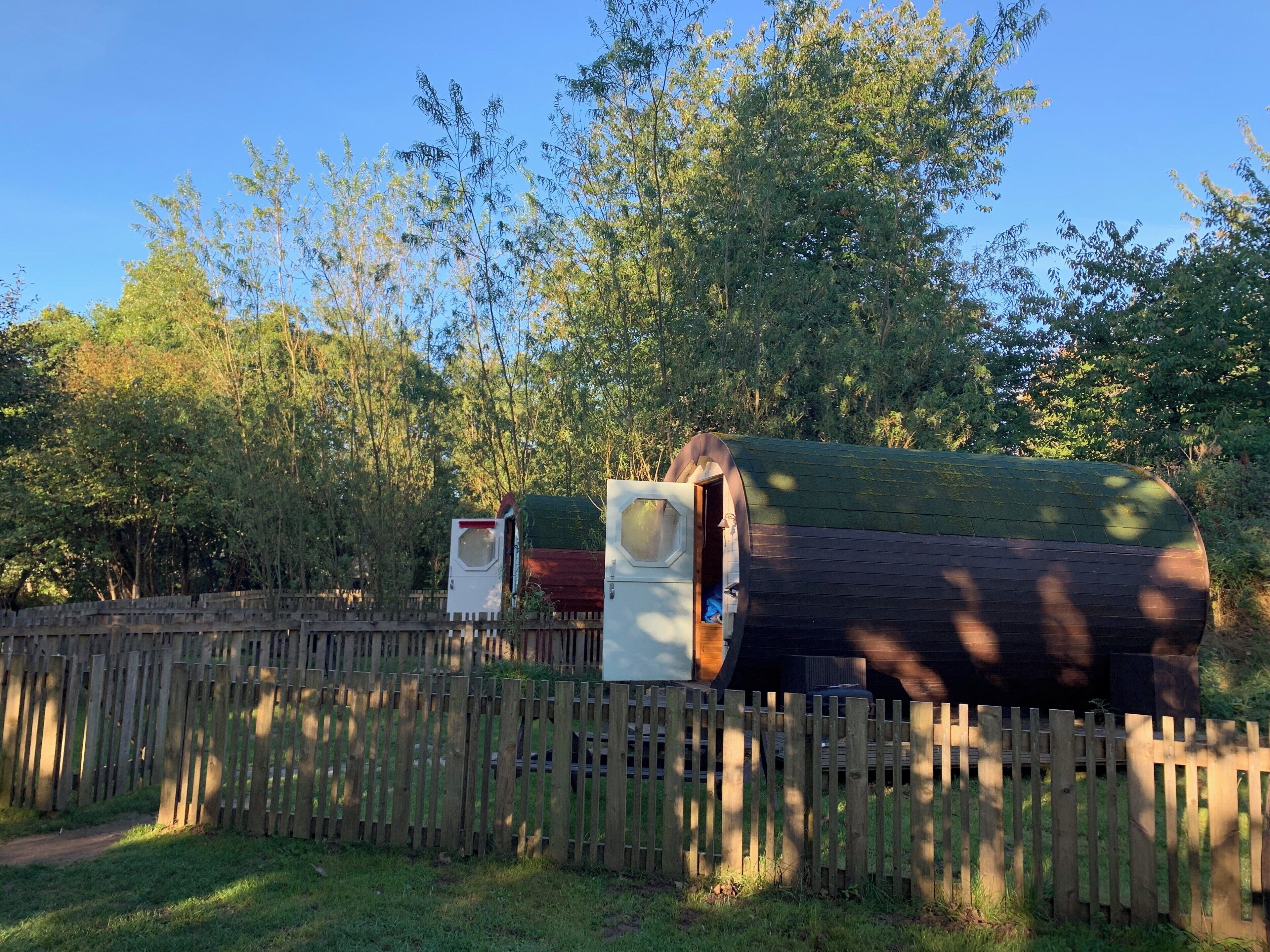 A wooden fence, a large log cabin, and a small white structure in a wooded area.
