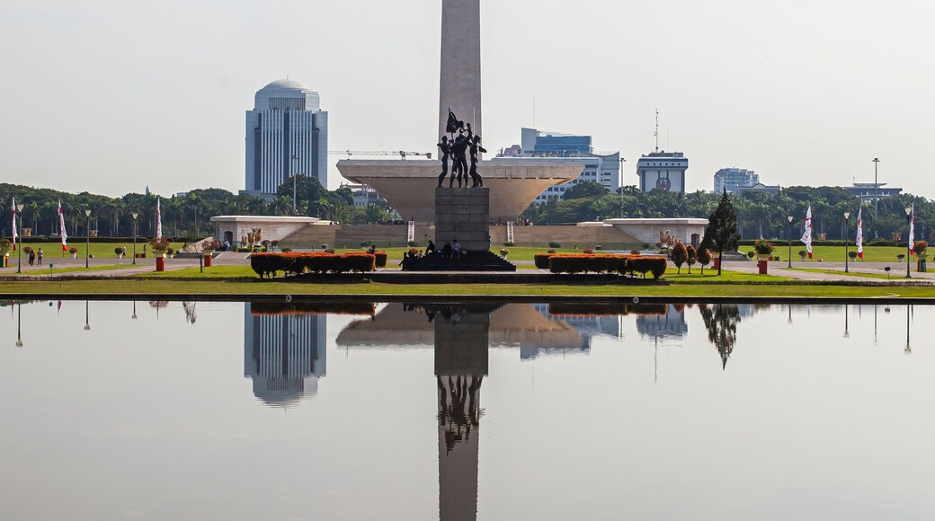 A tall monument with a statue at its base, surrounded by a reflective water body and greenery.