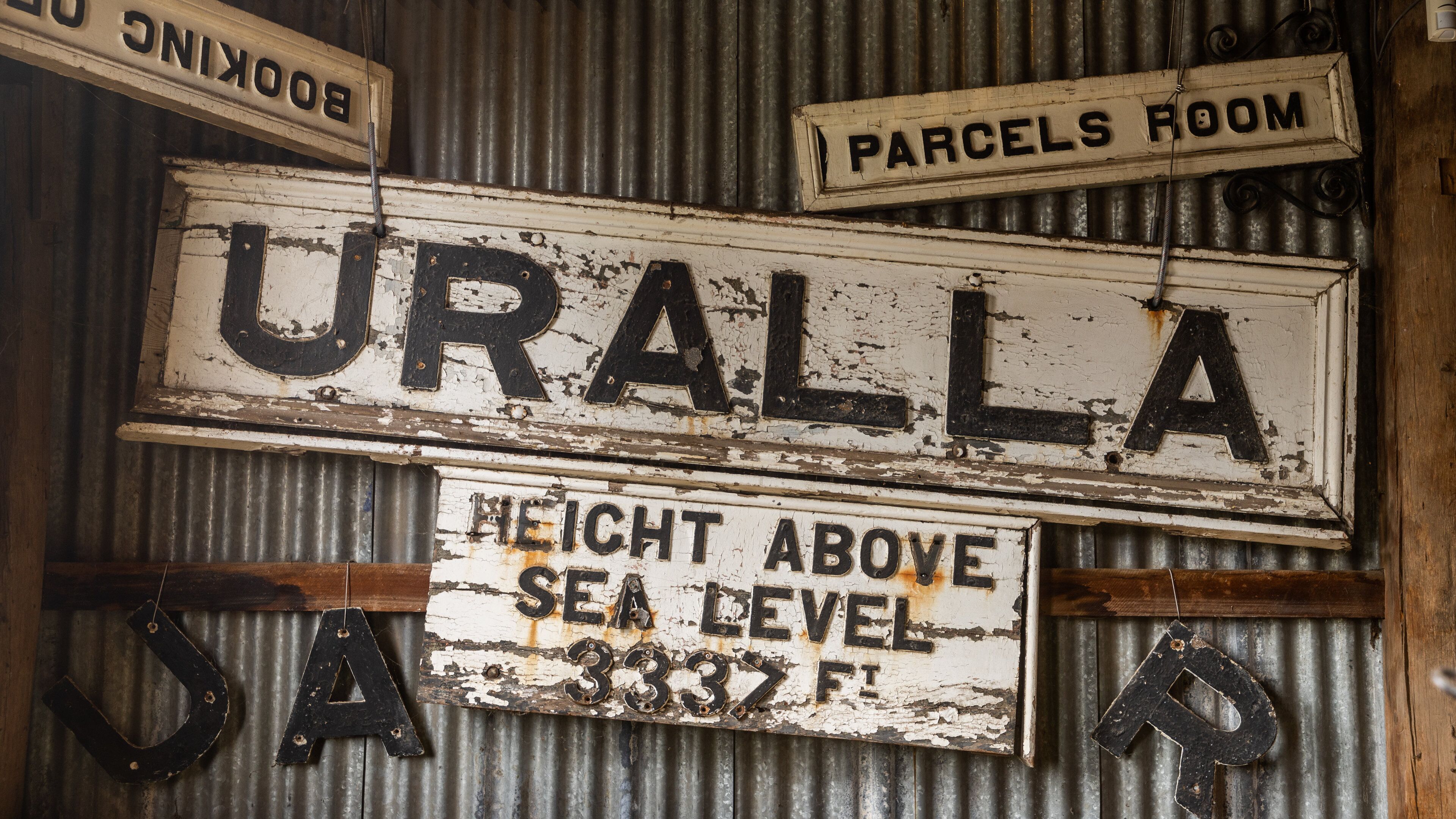 A weathered sign with 'URALLA' and 'PARCELS ROOM' above it, and 'HEIGHT ABOVE SEA LEVEL 3337 FT' below.