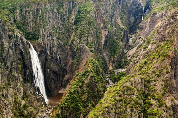 A waterfall cascading down a steep cliff surrounded by dense greenery.
