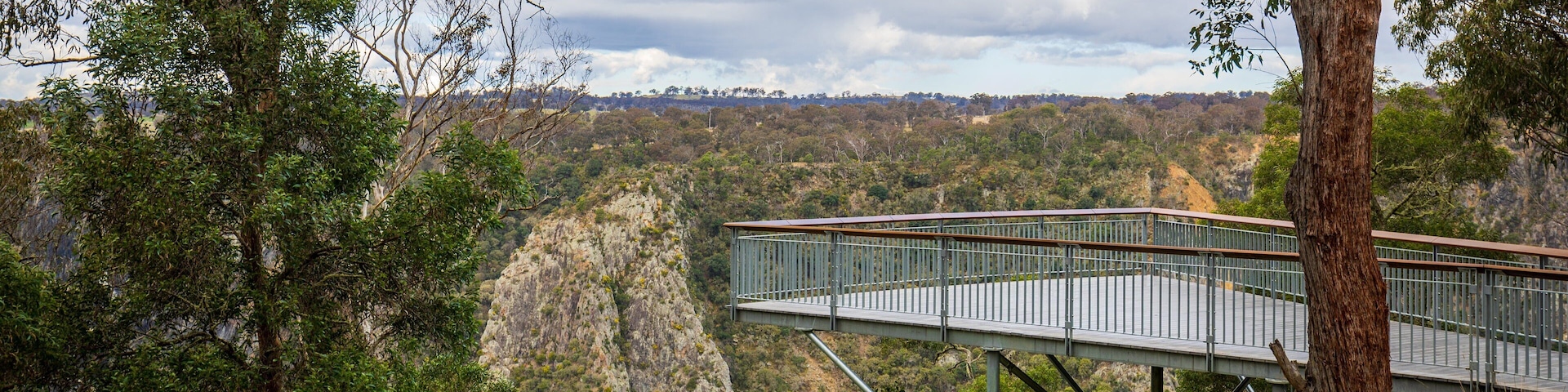 Uma plataforma de madeira com vista para uma paisagem montanhosa com vegetação densa e falésias rochosas.