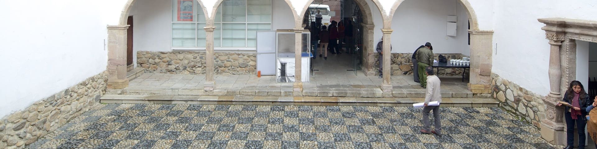 A courtyard with a tiled floor, arched doorways, and a balcony with railings.