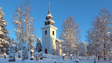 A snow-covered church with a steeple, surrounded by snow-laden trees and gravestones.