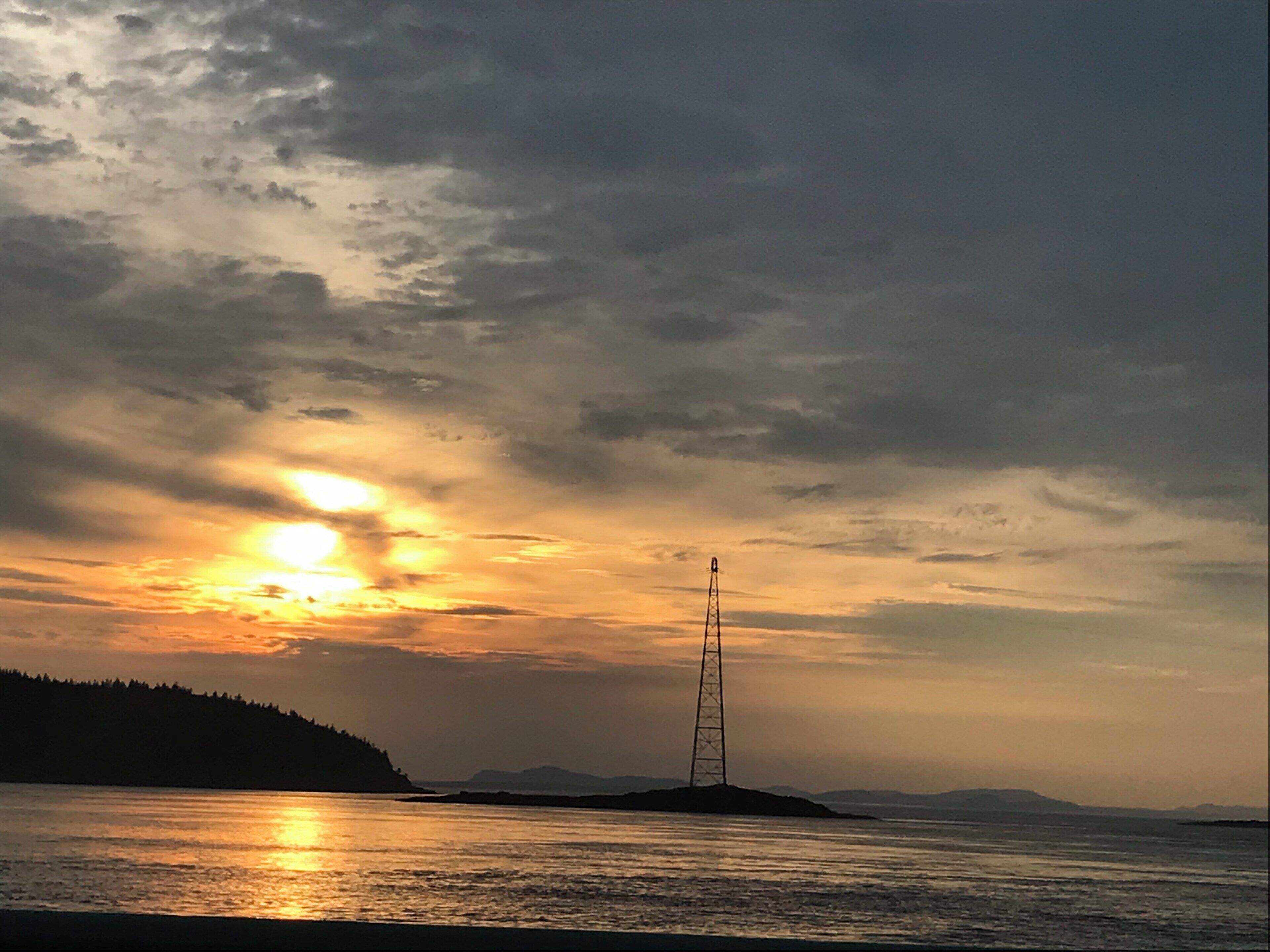A sunset over a calm sea with a transmission tower on an island.