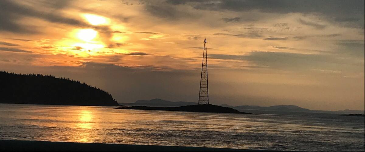A sunset over a calm sea with a transmission tower on an island.