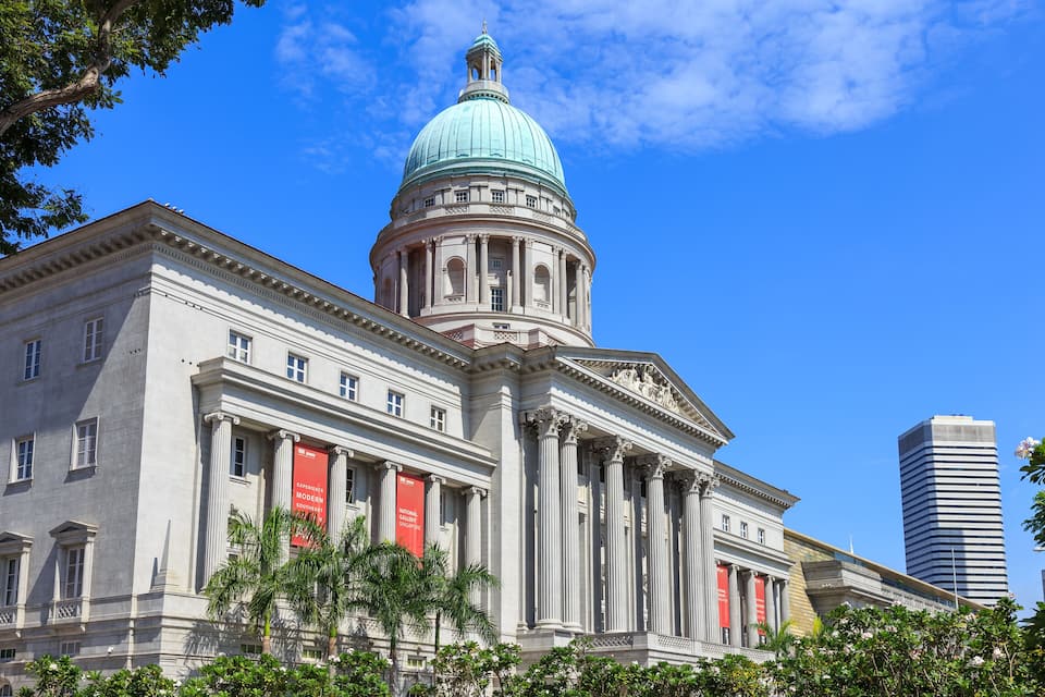 A classical building with a large dome and columns, a red banner, and a modern skyscraper in the background.