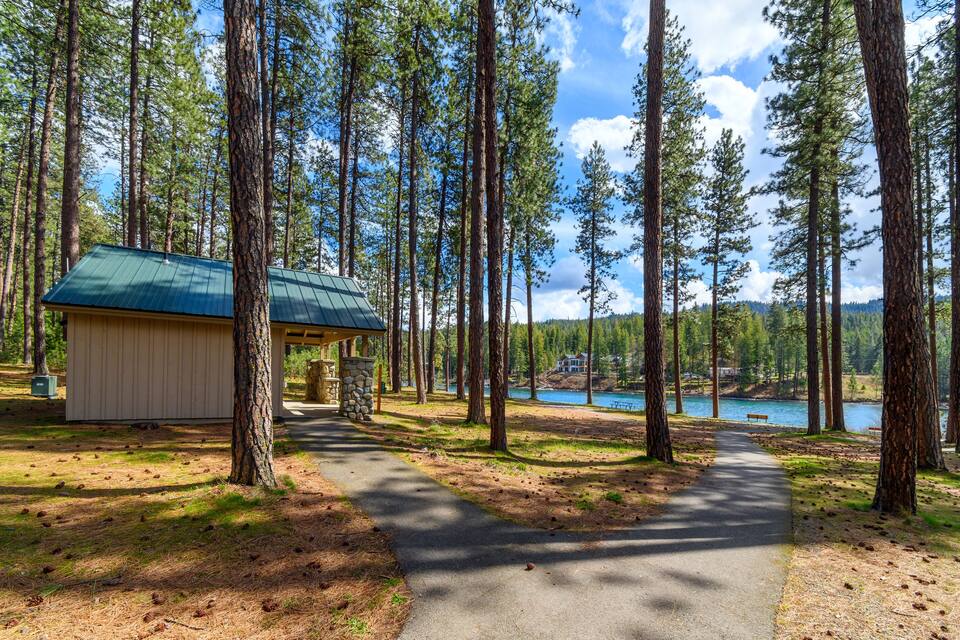 A forested area with a cabin, a lake, and a clear sky.