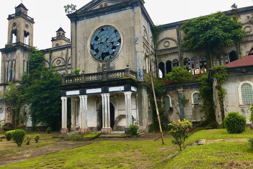 An old, ivy-covered building with a large circular window and a smaller clock tower.