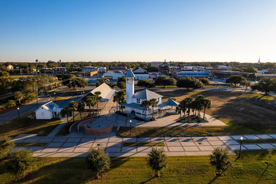 An aerial view of a town with a prominent white church, a clock tower, and a large statue in the center.