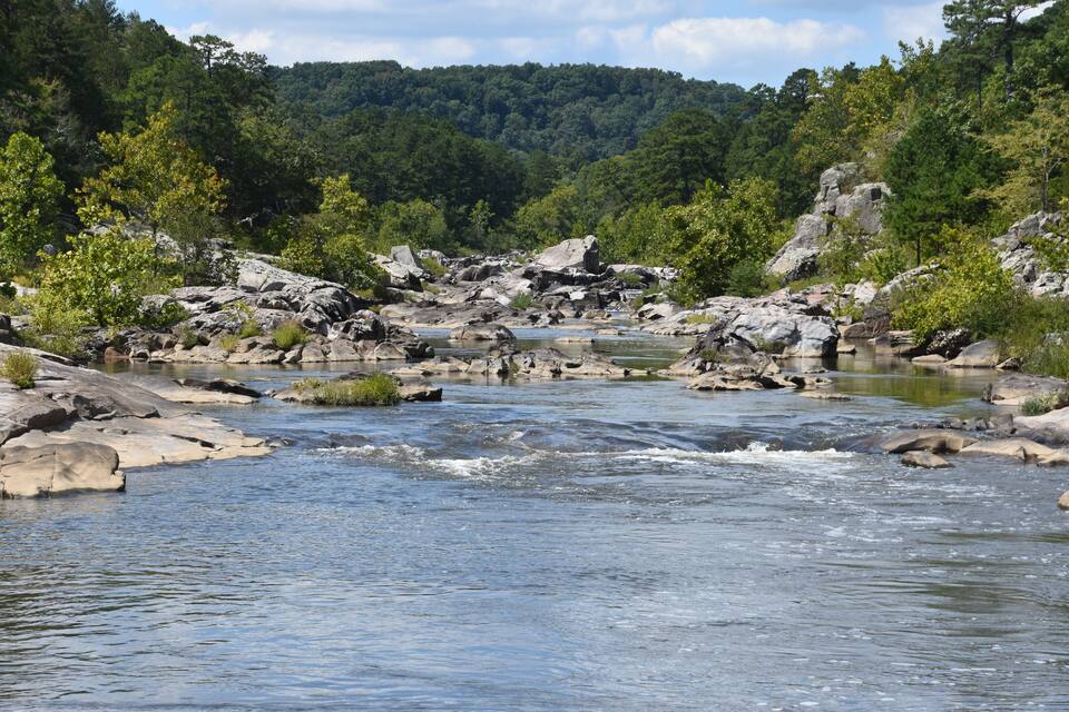 Une rivière qui traverse un paysage rocheux, avec des arbres et des collines en arrière-plan.