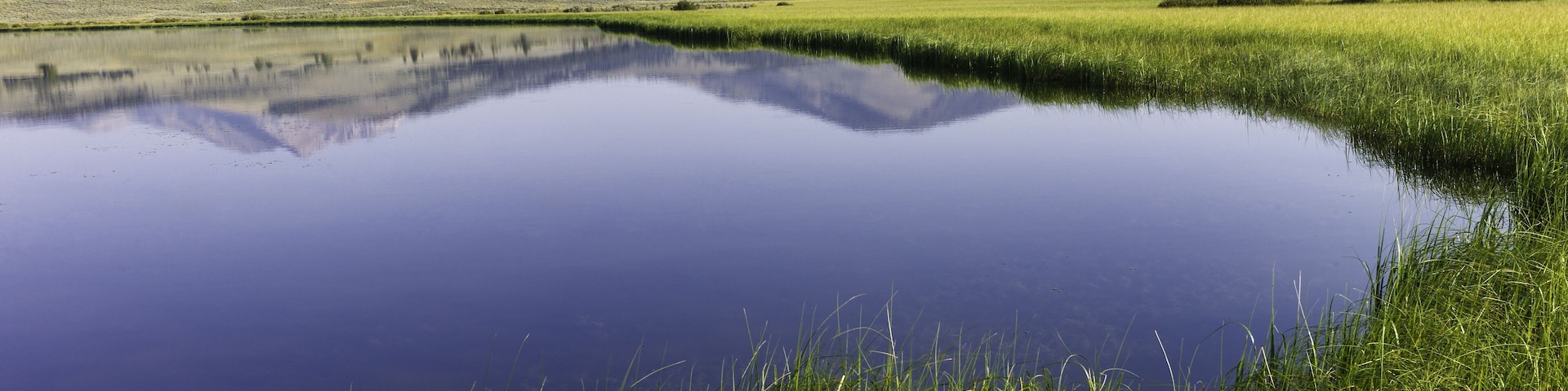 West Yellowstone, Wyoming, USA - Reflections of hills, trees, snow peaked mountains on a bring sunny day in Yellowstone National Park near West Yellowstone, Wyoming, USA.