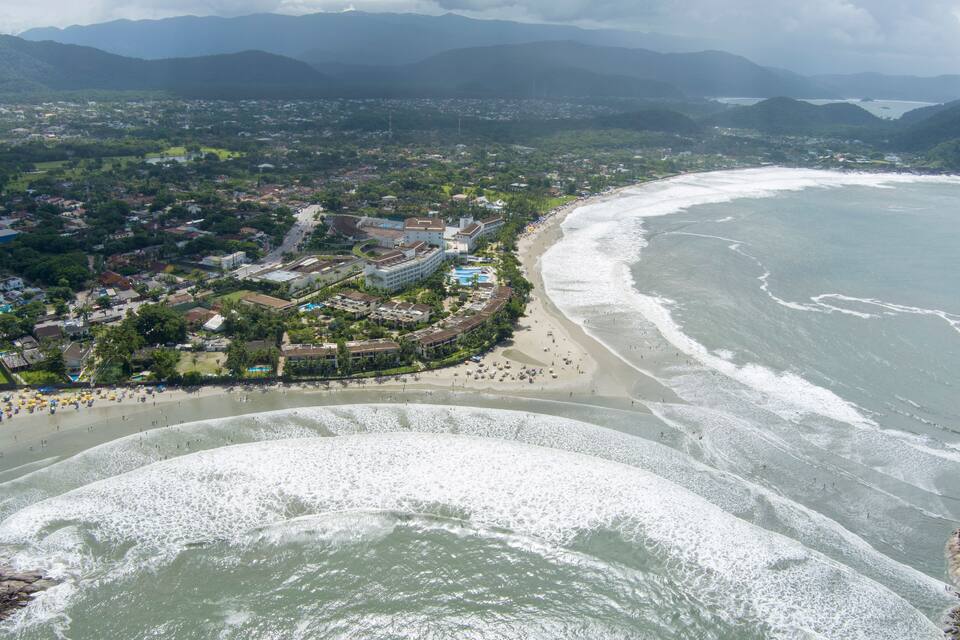 Un pueblo costero con una playa, olas del océano y montañas al fondo.