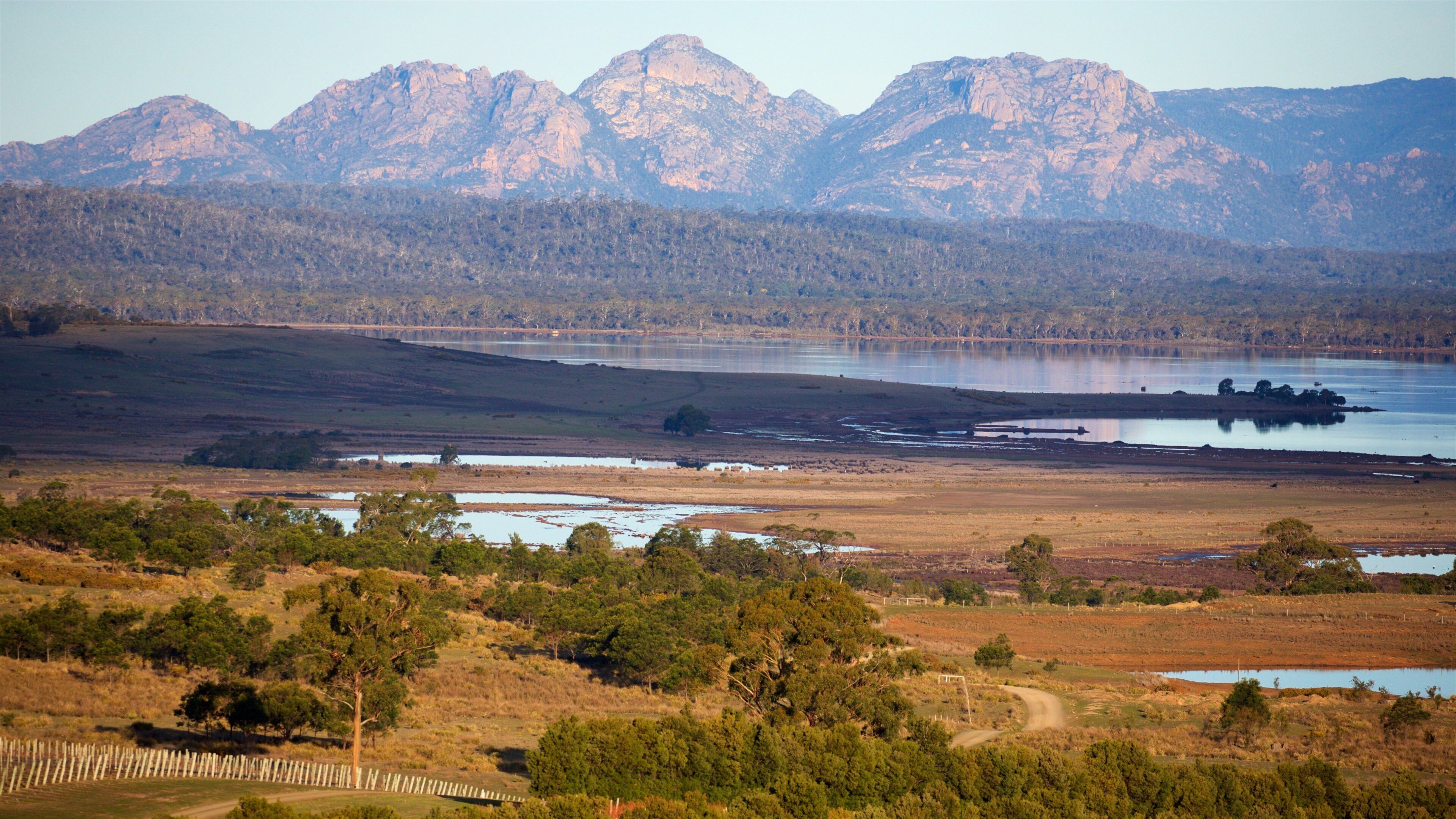 A landscape with a lake, mountains, and a dirt road.