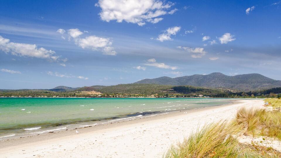 A beach with clear turquoise water, white sand, and green hills in the background.