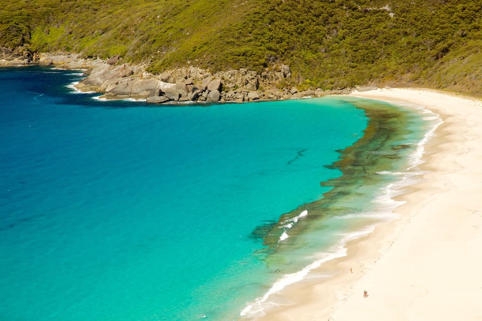 A turquoise beach with clear waters, sandy shore, and rocky coastline.