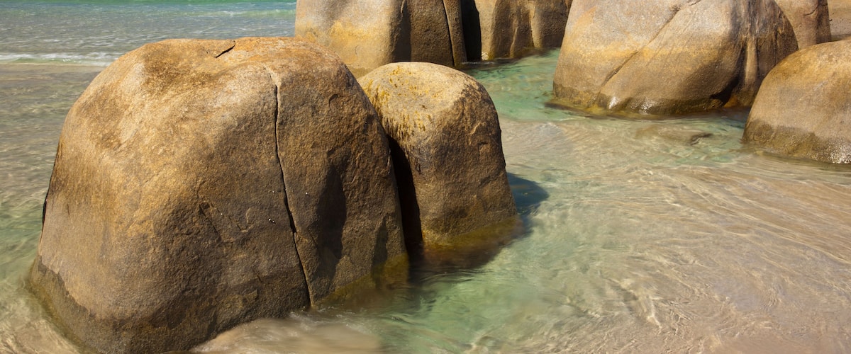 Large boulders in shallow water with clear turquoise sea and a clear blue sky.