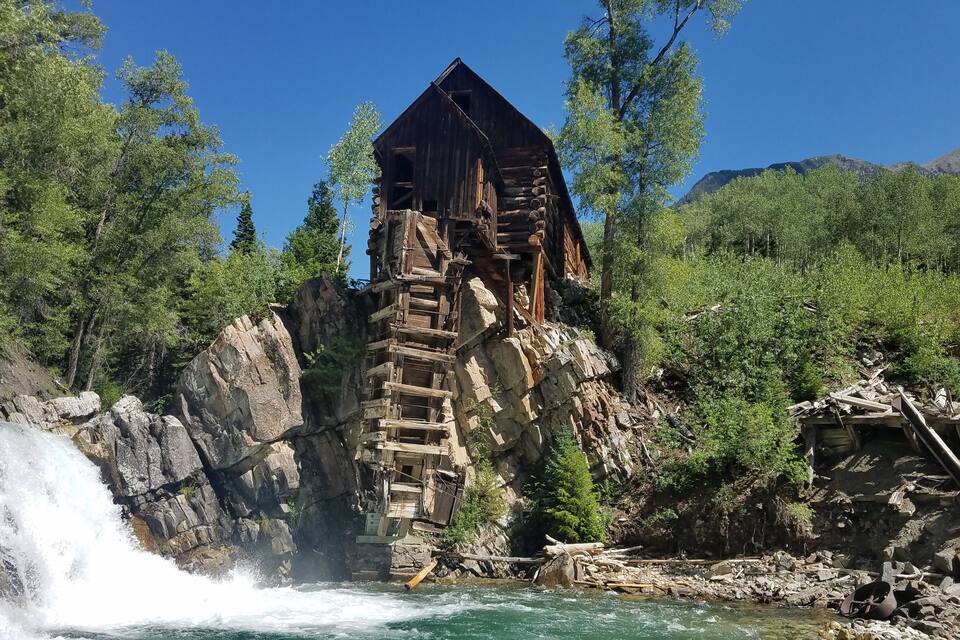 A wooden watermill with a waterfall in a forested area.